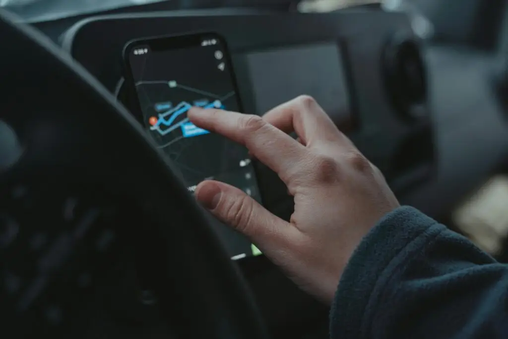 Hand interacting with GPS navigation on a smartphone mounted in a car interior.
